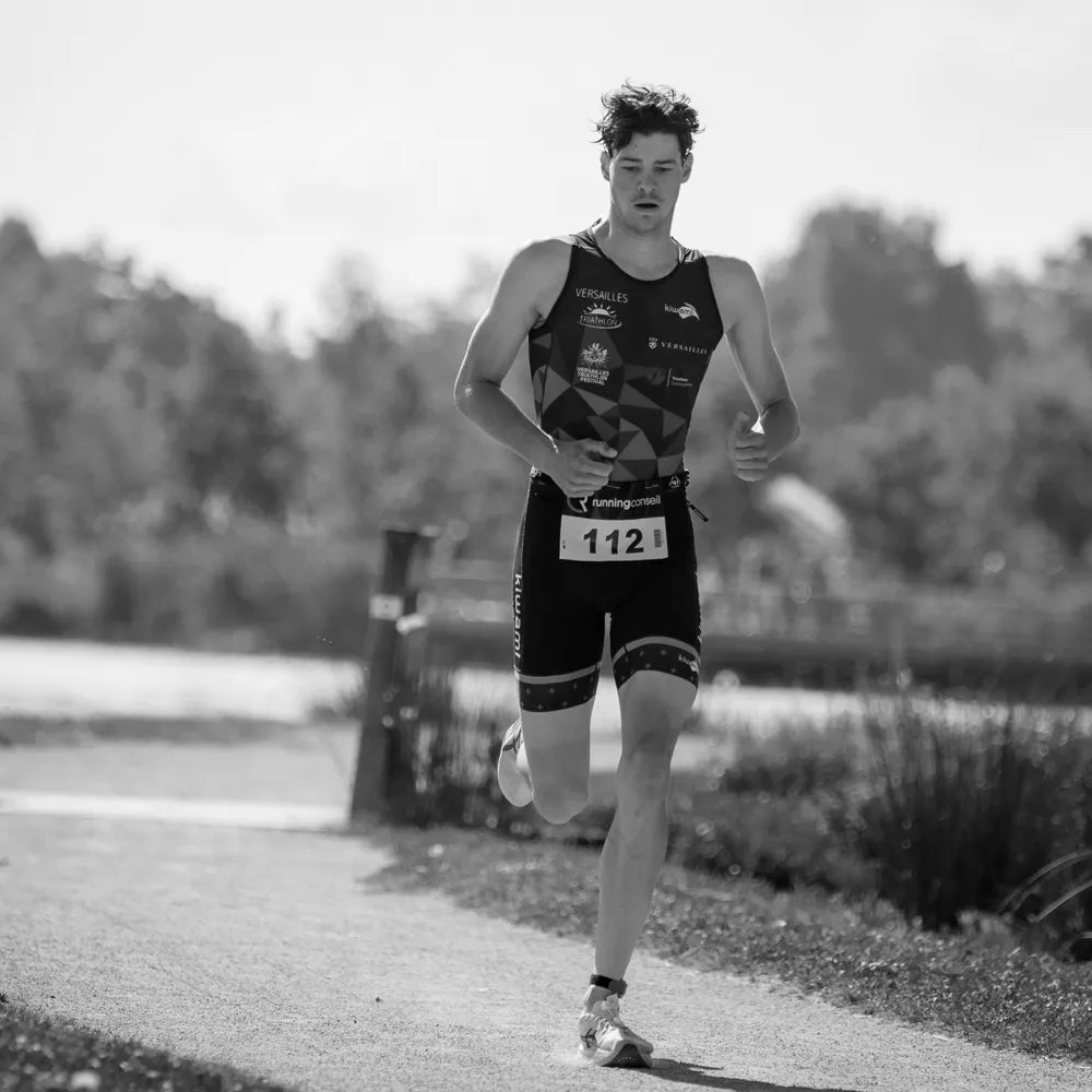 Athlète de triathlon en course à pied avec dossard, épreuve de running en pleine nature au bord d'un lac