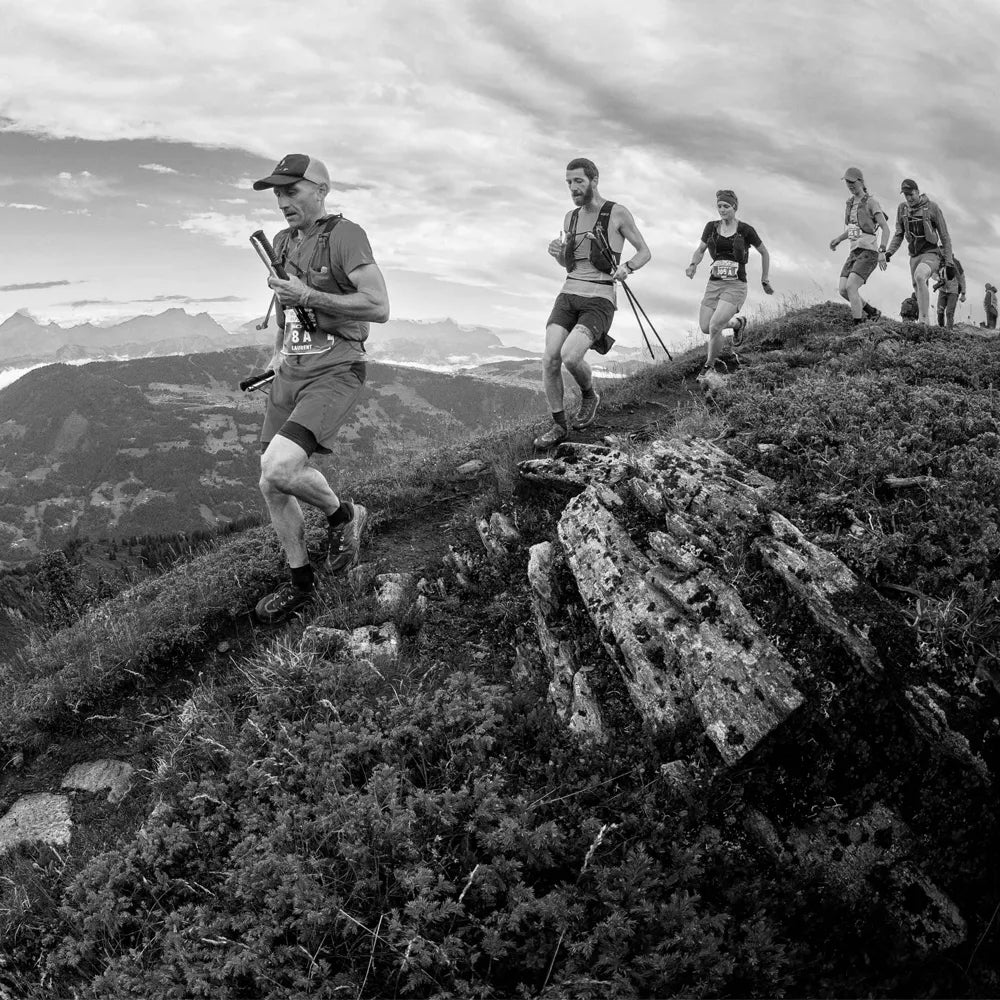 Groupe de traileurs en file avec bâtons, courant sur une crête herbeuse en haute montagne