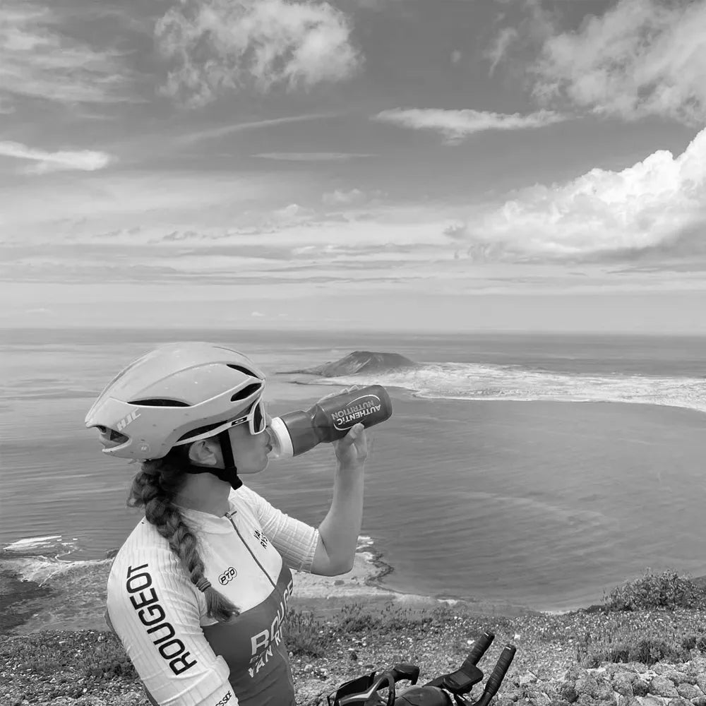 Cycliste avec casque Rougeot buvant à son bidon lors d'une pause face à la mer, illustrant l'hydratation sportive.